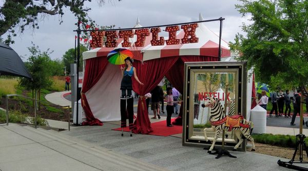 A circus-like entrance with someone on stilts, a wooden zebra, and the word Netflix in bright lights.